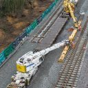 From above, two heavy rail-mounted cranes lower a track section into place