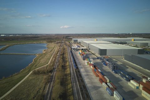Drone shot of iPort Rail at Doncaster looking down the tracks at a departing intermodal train, The reservoirs are on the left, and warehouses on the right